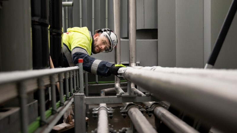 testovanie plynu a zisťovanie úniku plynu - muž v pracovnom odeve a v ochrannej čiapke pracuje na potrubnom systéme.