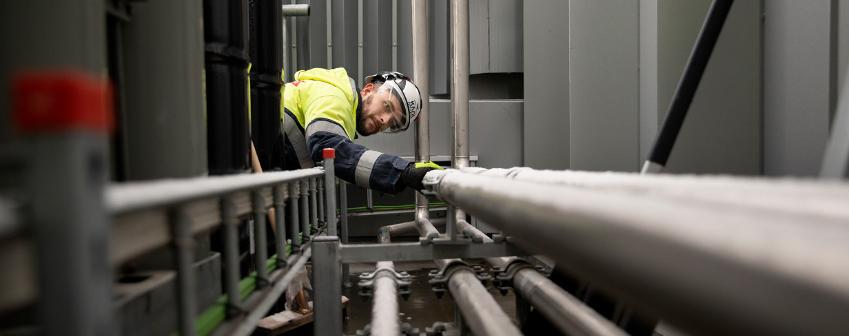provtryckning med gas och läcksökning med gas – en man i arbetskläder och skyddshjälm som arbetar med ett rörsystem.